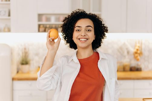 Joyful woman embarking on keto and intermittent fasting journey with an orange in hand