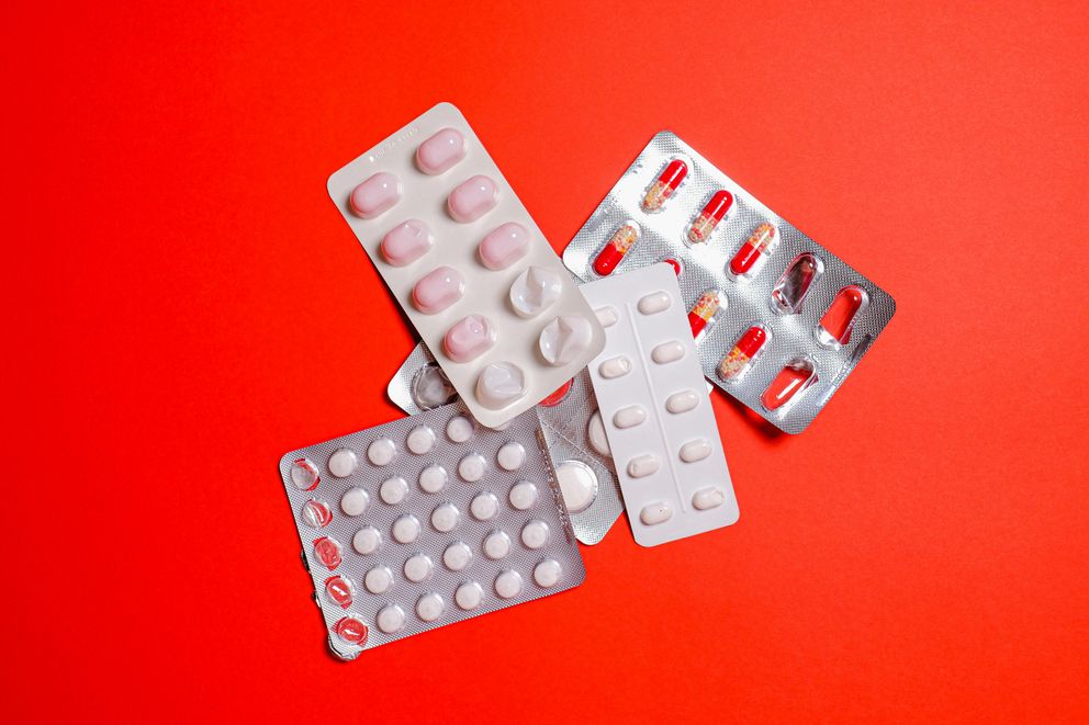 Various painkiller pills scattered next to a smartphone displaying an intermittent fasting app, illustrating the question of whether painkillers interfere with fasting.