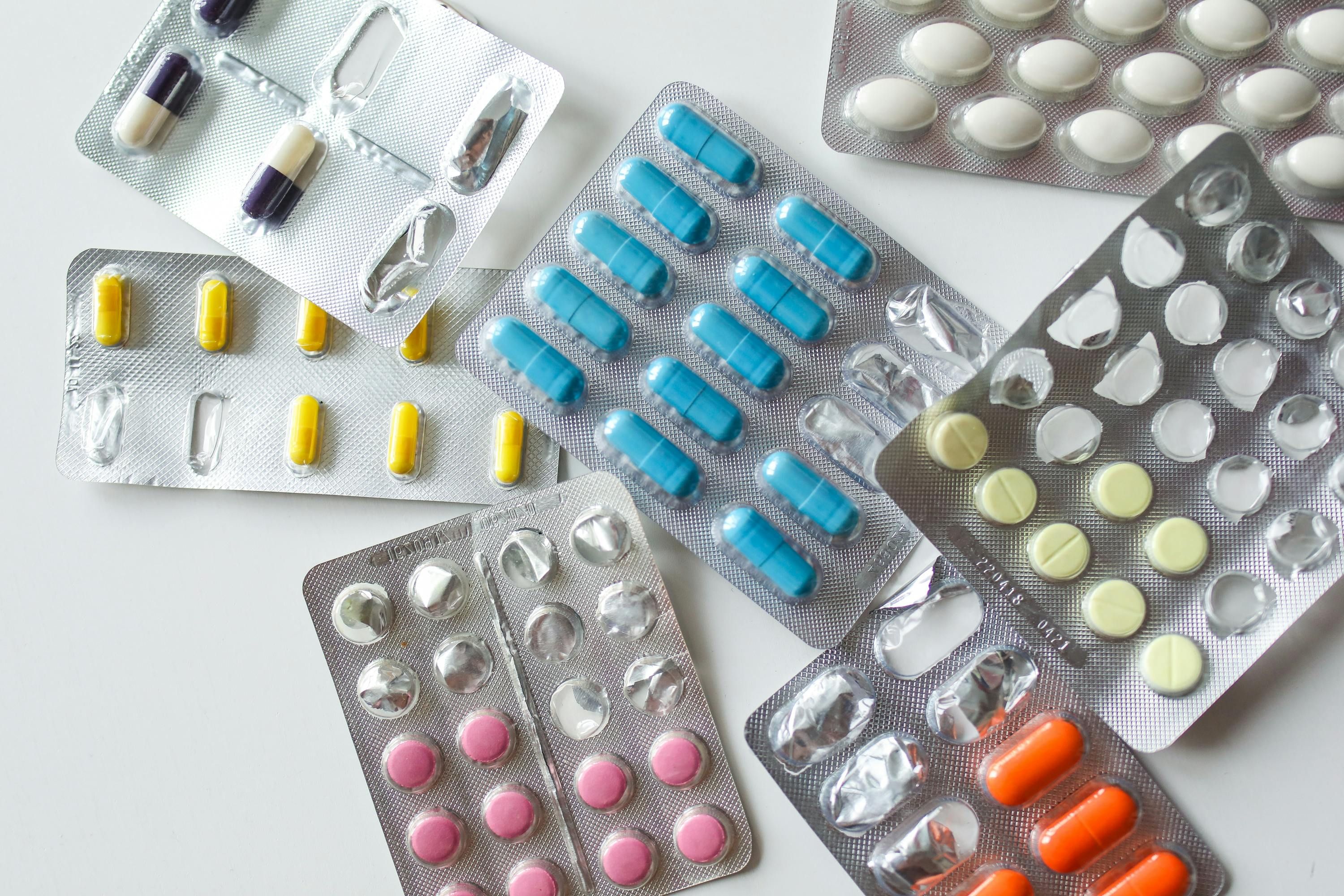 Various common painkillers scattered on a table next to a smartphone displaying an intermittent fasting app timer