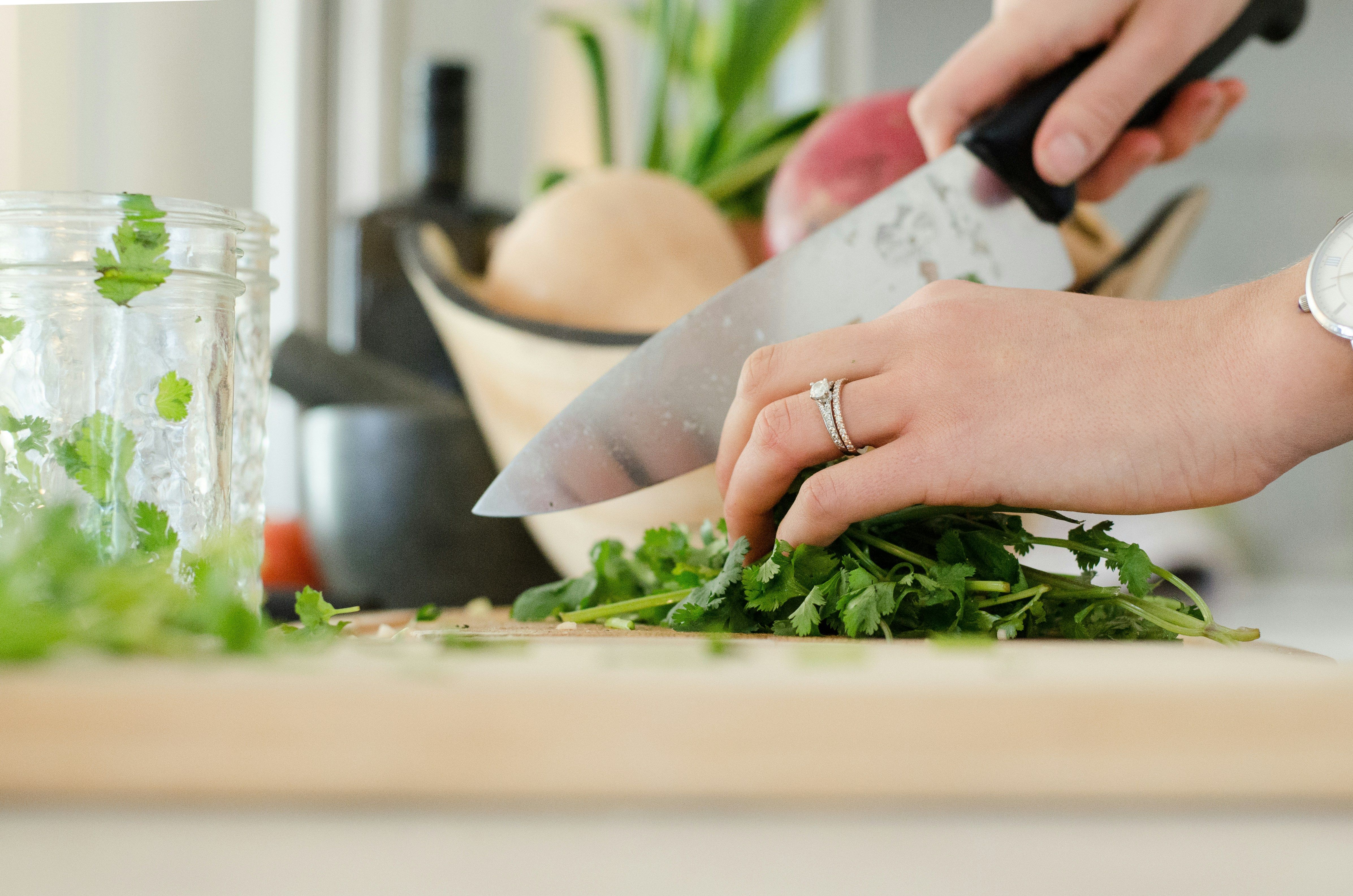 A woman joyfully preparing healthy meals in her kitchen, chopping fresh vegetables and herbs.