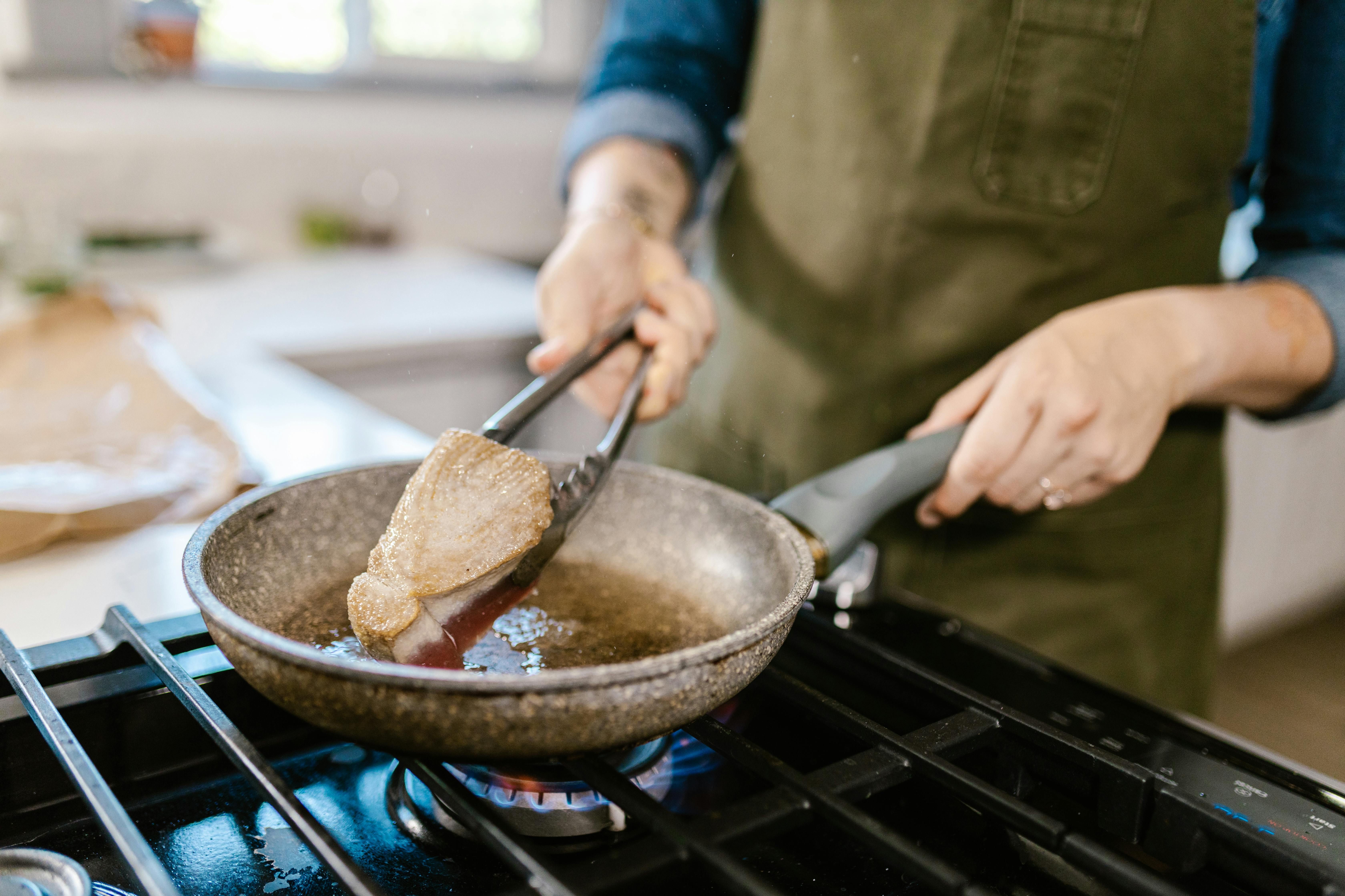 A woman frying meat in a pan on the stove.