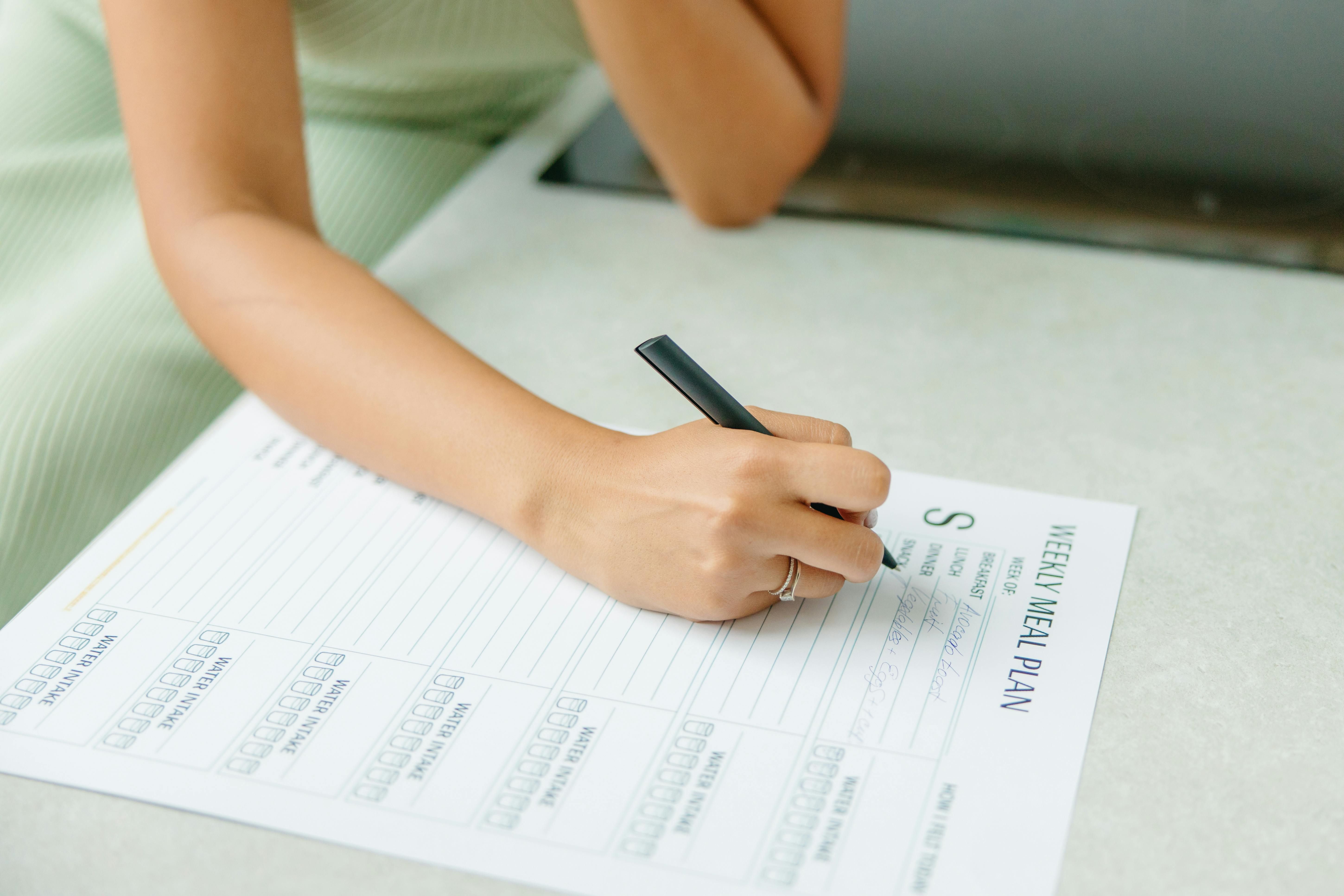 A woman planning her weekly meals at a kitchen table with a notebook and fresh ingredients.